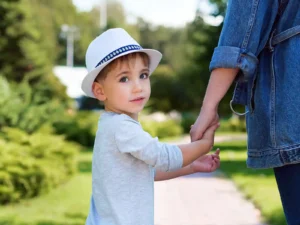 Žena drží za ruku chlapca, ktorý sa pozerá za seba do objektívu